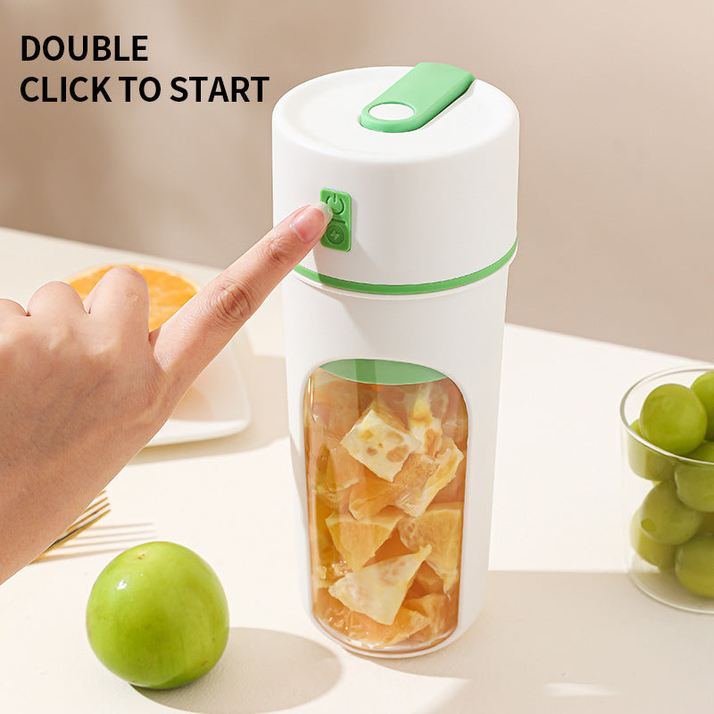 Hand pressing a button on a white and green electric juicer with fruits around.