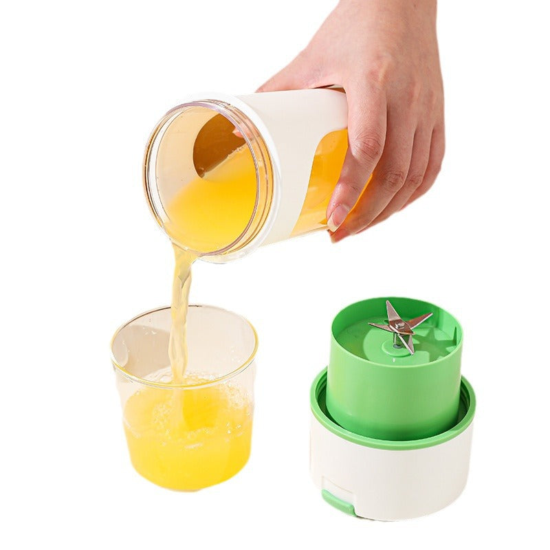 Hand pouring juice from a container into a glass with a green and white blender on a white background