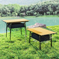 Two folding camping tables by a lake showing low and high height and table dimensions
